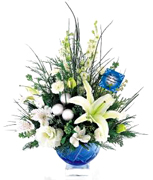 Miami Christmas: Oriental lily, larkspur and lisianthus, all in shades of winter white, make this holiday centerpiece an elegant yet festive statement. Accented with seasonal greens, eucalyptus stems and silver glass balls, its beautifully presented in a blue cut-glass bowl with a distinctive clear, block base. This blue bowl sizes 6 1/2" dia. x 4 1/2"H